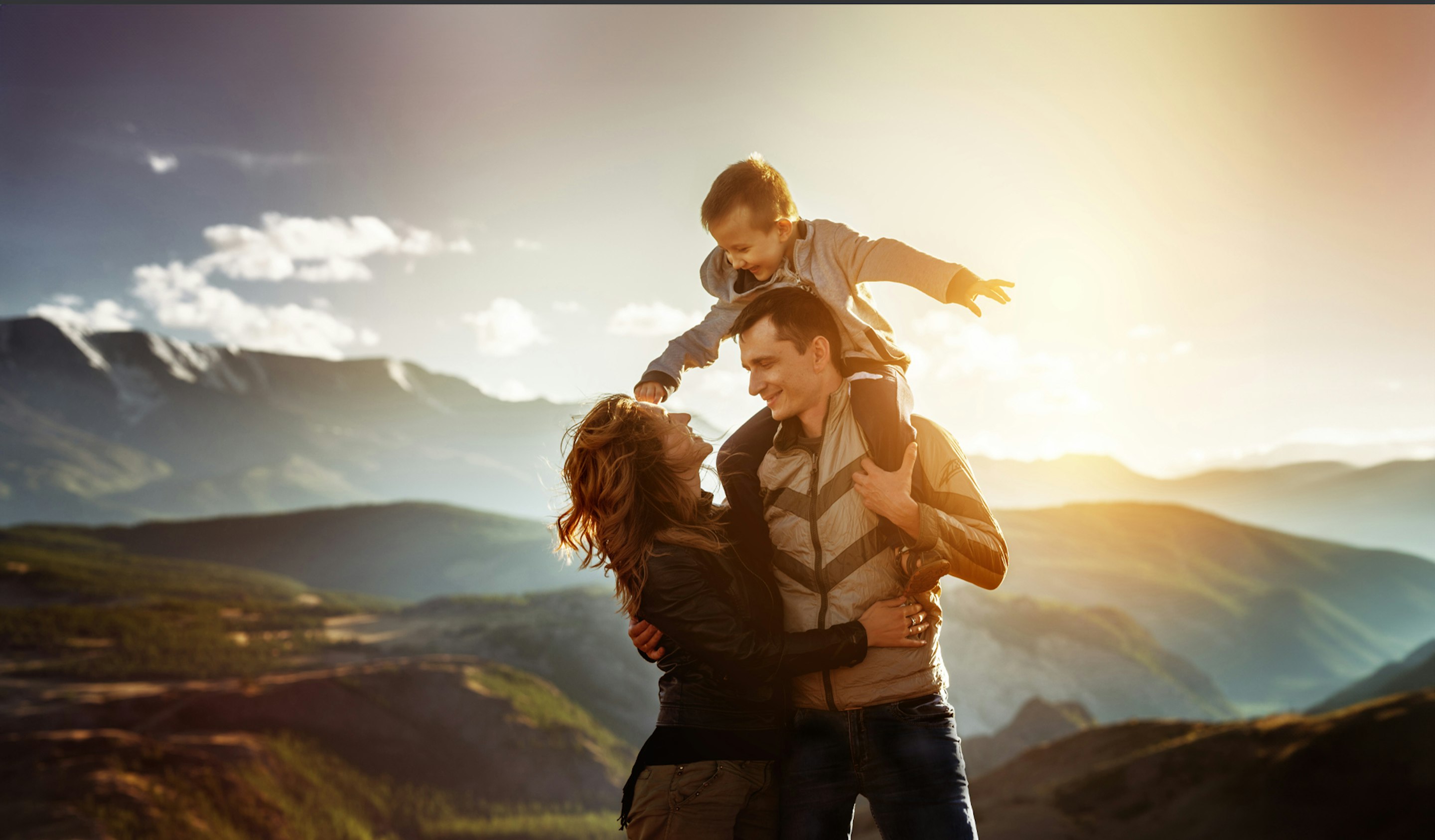 Eine Familie seht auf einem Hügel und sehen sich die Berge vor ihnen an. Der kleine Junge sitzt auf den Schultern des Vaters. Sorgen auch Sie vor und sparen Sie in Edelmetalle, mit den Sparplänen von Golden Gates.