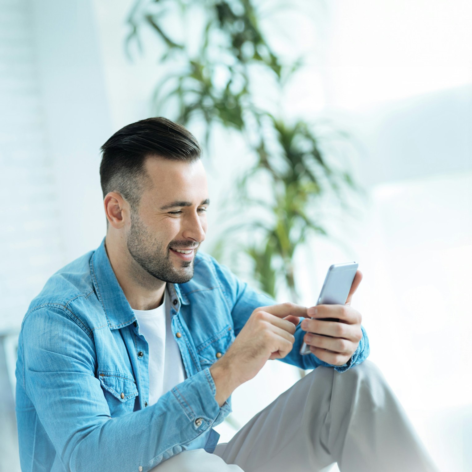 In einem hellen Raum sitze ein Mann und sieht strahlend auf sein Handy, in seiner Hand. Legen auch Sie Ihr Geld richtig an und sparen Sie in Anlagemetalle mit den Sparplänen von Golden Gates.