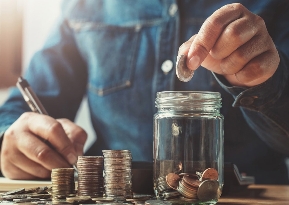In einem hellen Raum sieht man, an einem Tisch eine Person sitzen. Diese zählt Münzen und schreibt die bestände auf. Sparen Sie Ihr Geld mit der Chance auf Wertsteigerung, mit den Edelmetallsparplänen von Golden Gates.