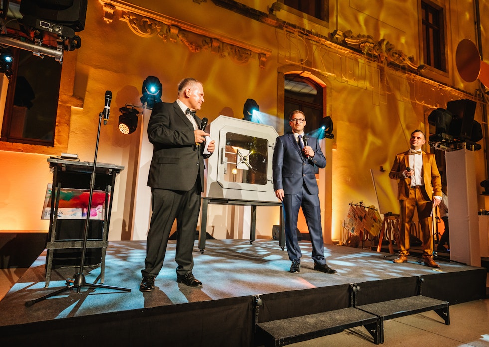 Auf der Tribüne stehen die Gründer der Golden Gates Edelmetalle AG, Herbert und Constantin Behr, und eröffnen die Jubiläumsfeier „10 Jahre Golden Gates“.