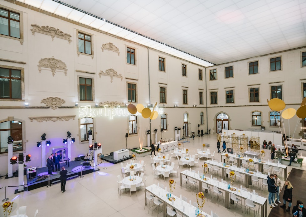 Festsaal im Albertinum. Hier stehen, in einem großen, hellem Raum, viele weiße Tische. In einer Ecke des Raumes ist ein Rednerpult aufgebaut.
