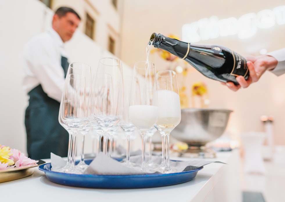 Champagner zum Anstoßen. Einer Person gießt Champagner in Sektgläser ein.