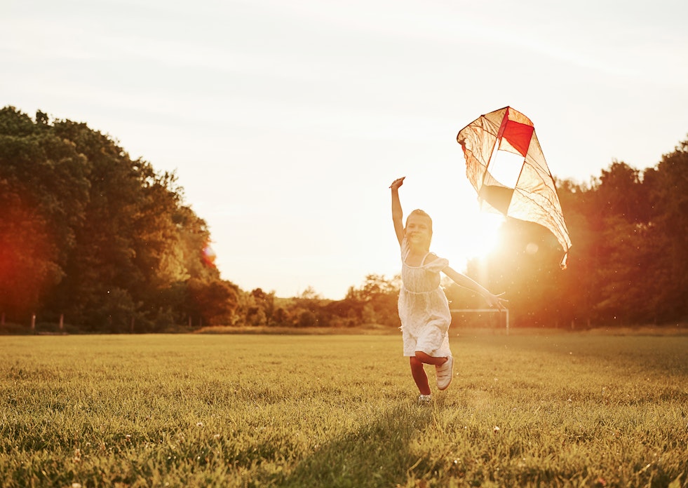 Auf einer großen Wiese, wo die Sonne hinter den Bäume hervorlugte, rennt ein glückliches Kind und lässt seinen Drachen steigen. Sorgen auch Sie für die Zukunft Ihres Kindes mit dem Kindersparplan von Golden Gates.